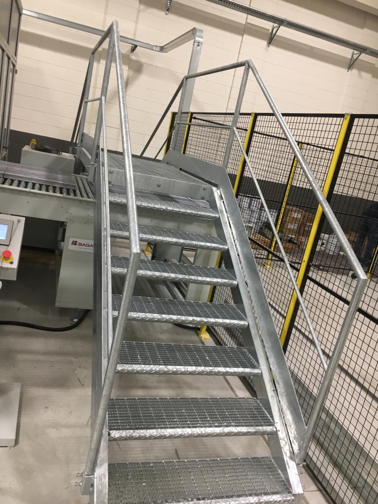 Scala metallica con gradini grigliati e corrimano all'interno di uno stabilimento industriale.