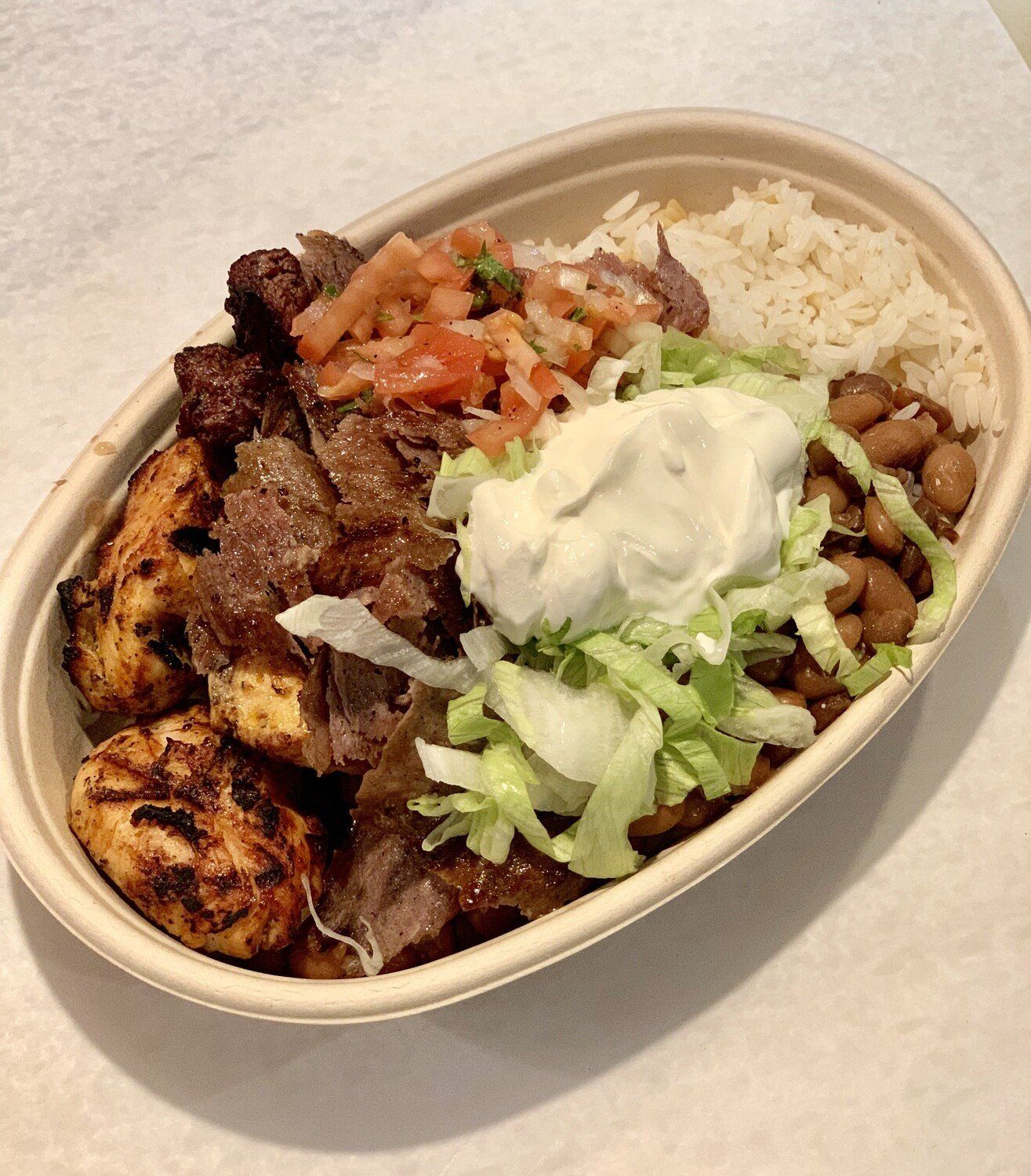 A bowl of food with rice beans lettuce and sour cream