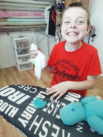 A young boy is mending a teddy bear and ironing an ear