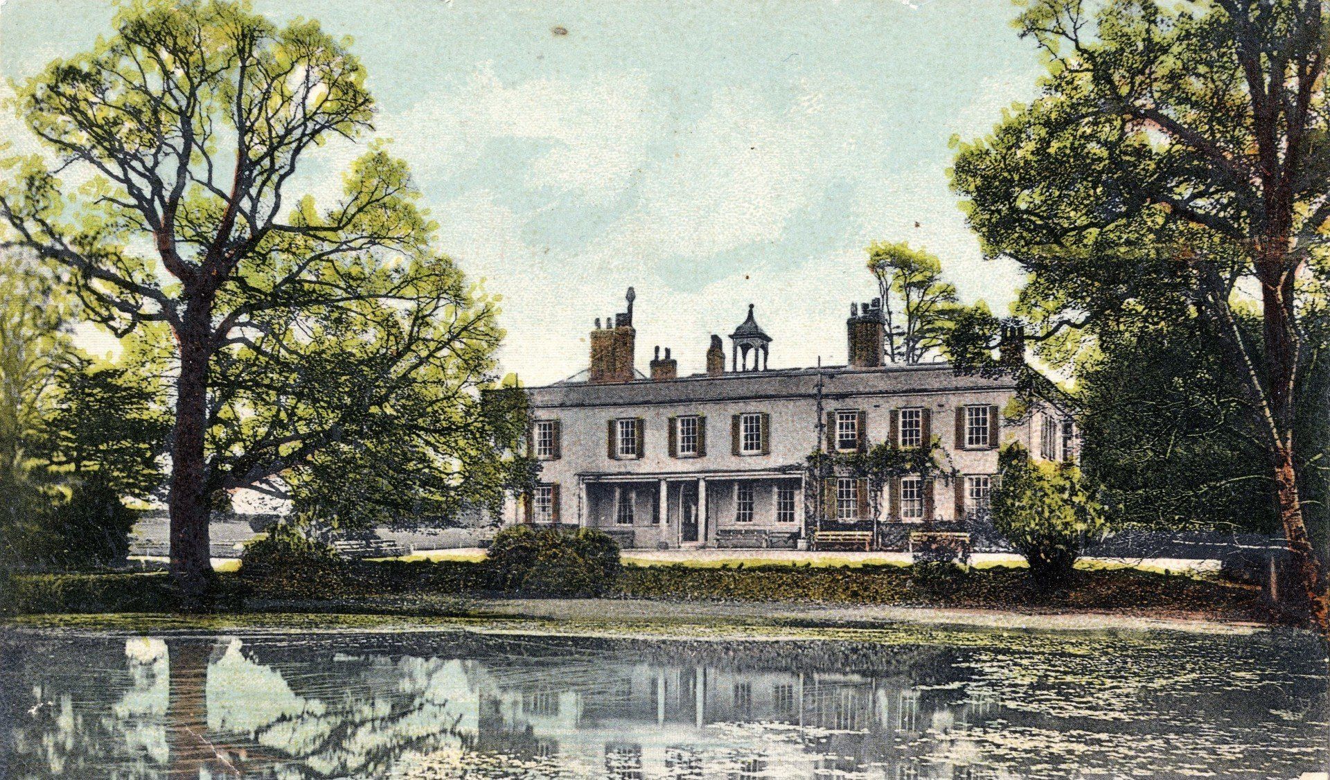 A large house is surrounded by trees and a body of water