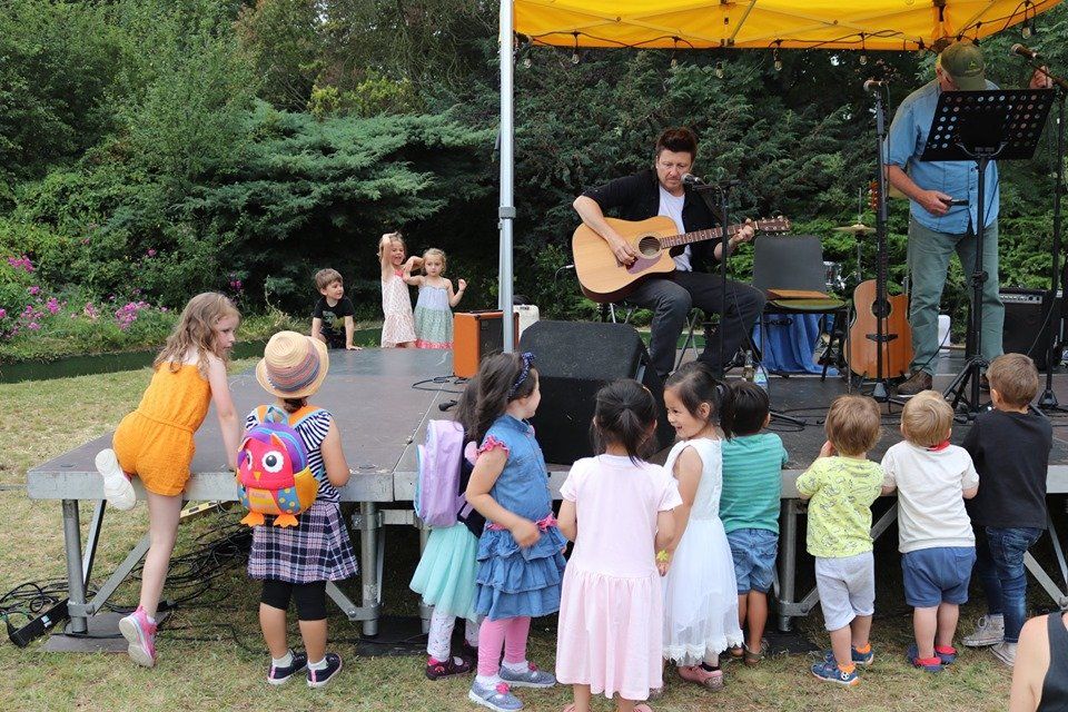 A group of children are standing on a stage watching a man play a guitar.