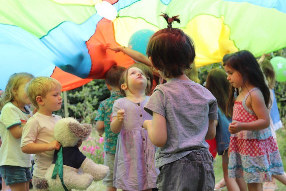 A group of children are playing under a colorful parachute.
