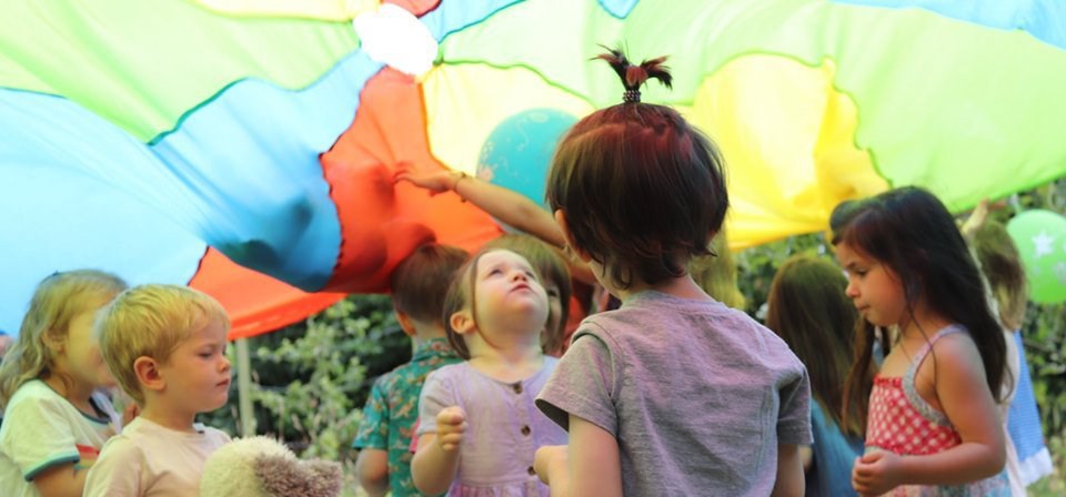 A group of children are playing under a colorful parachute.