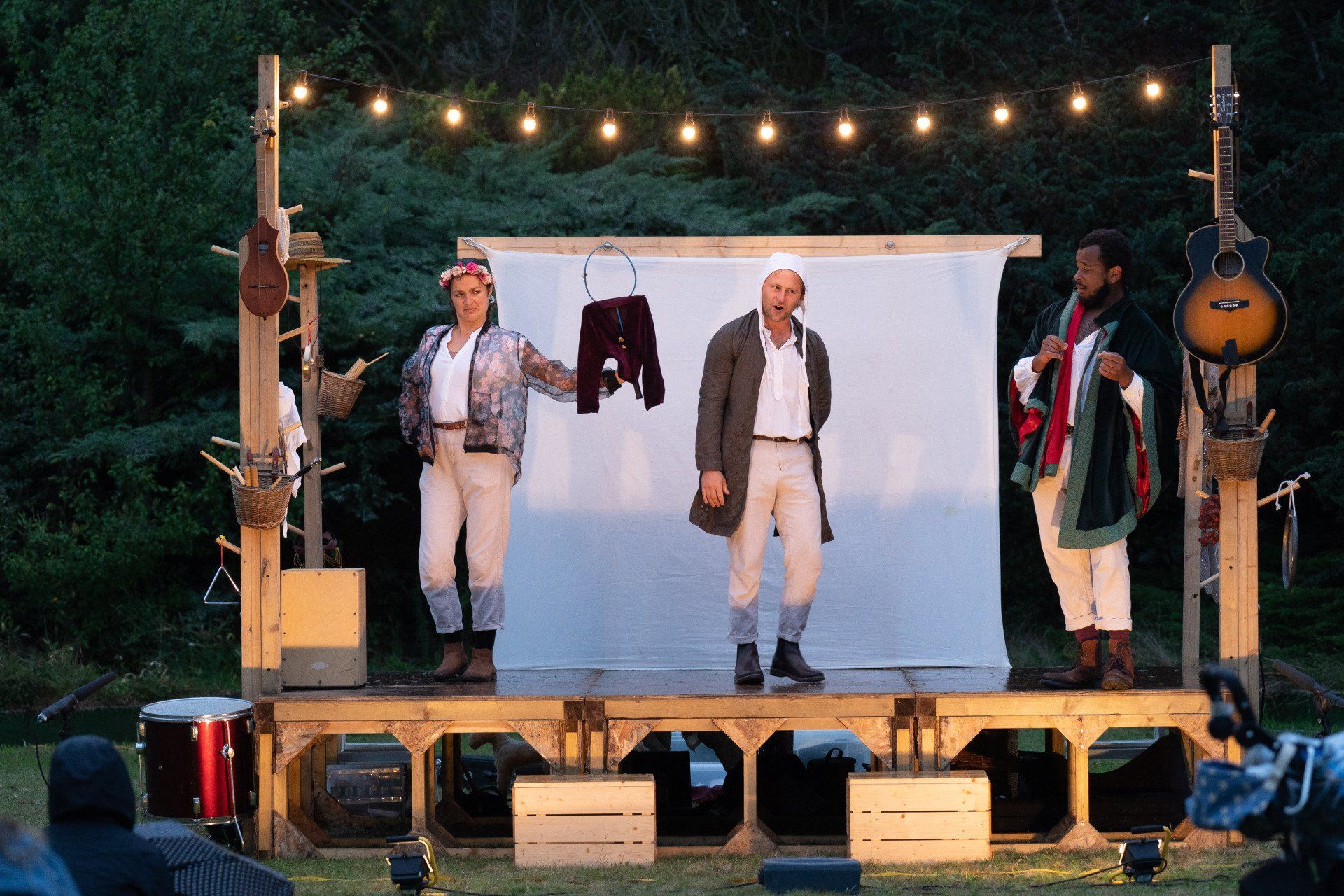 Three men are standing on a stage in front of a white wall.