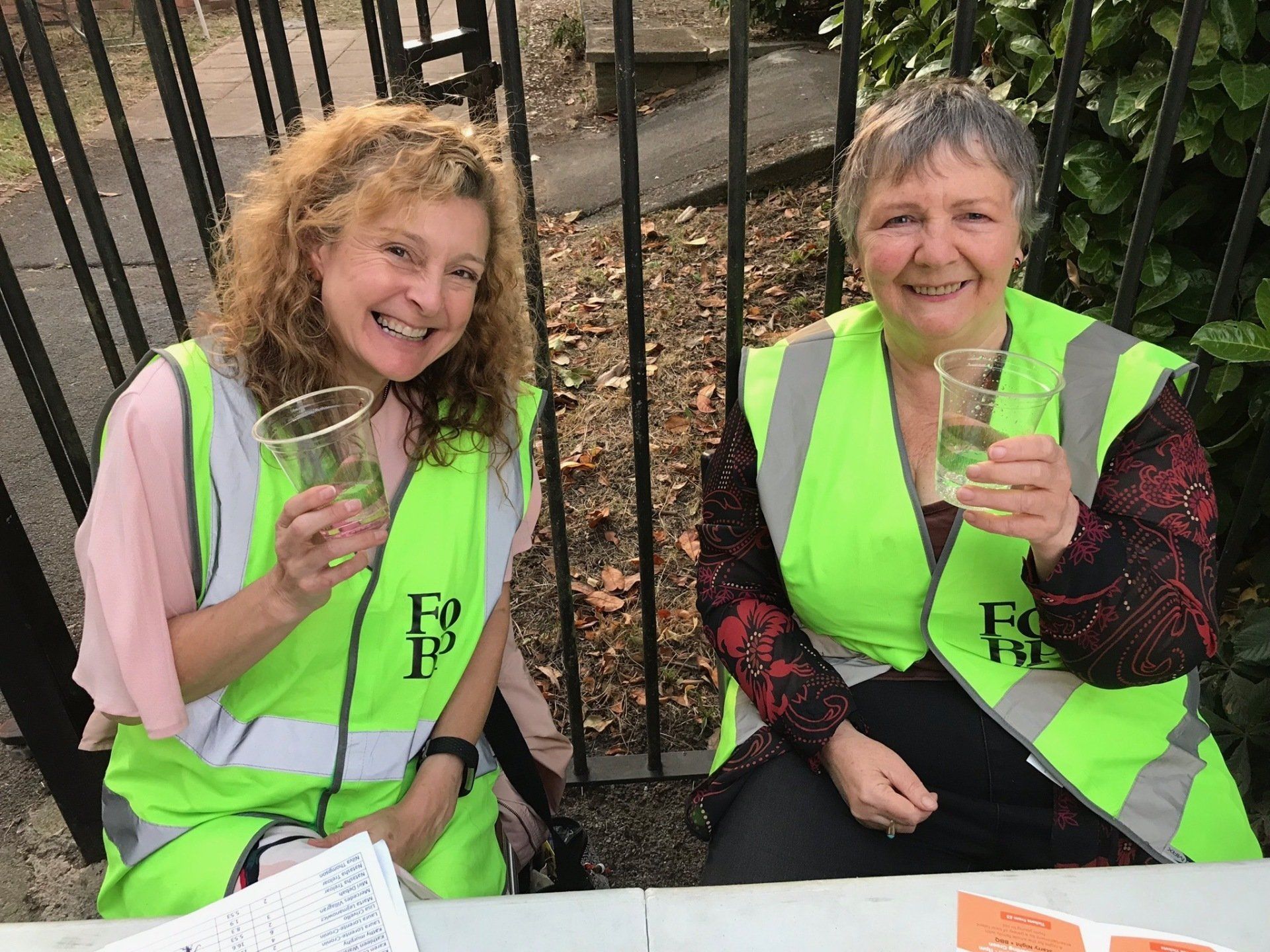 Two women in yellow vests are sitting at a table holding glasses of water.