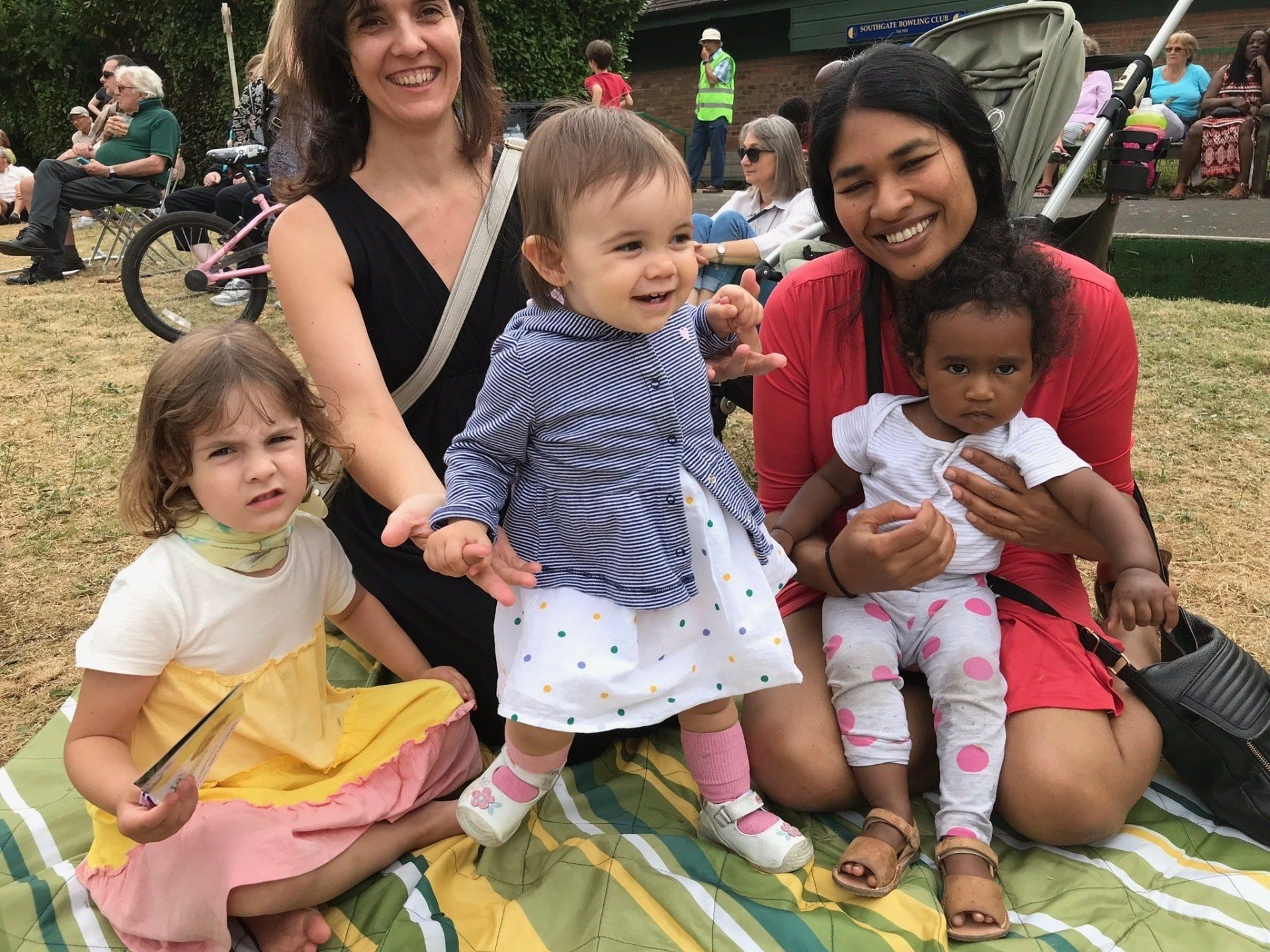 A group of women are sitting on a blanket with their children.