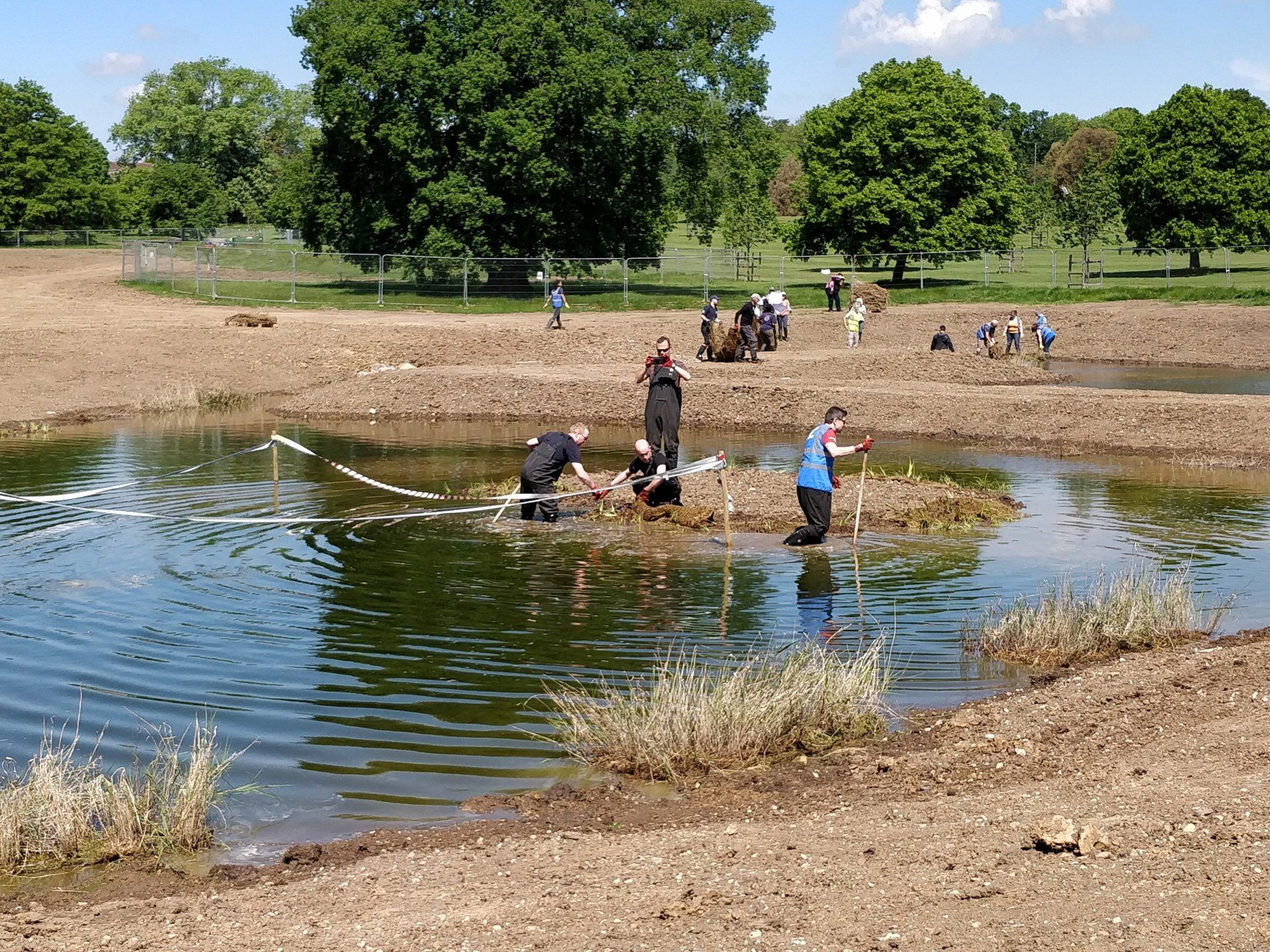 A group of people are standing on a small island in the middle of a pond.