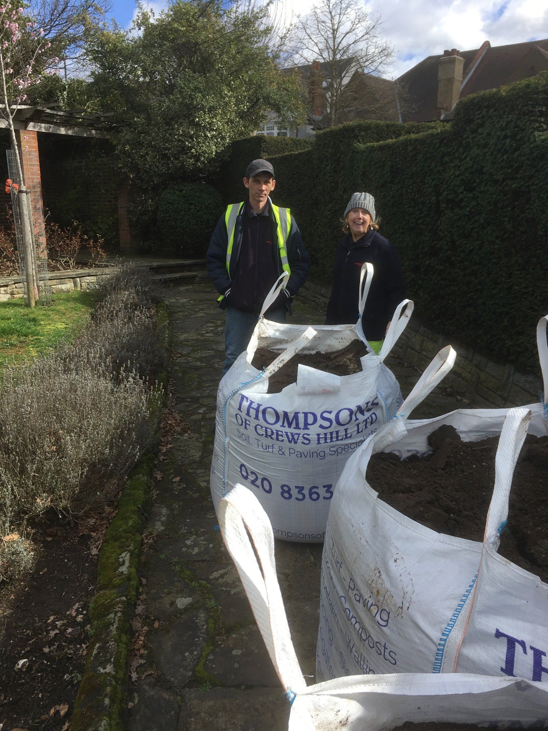 A man and a woman are standing next to bags of dirt.