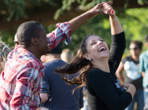 A man and a woman are dancing together in a park.