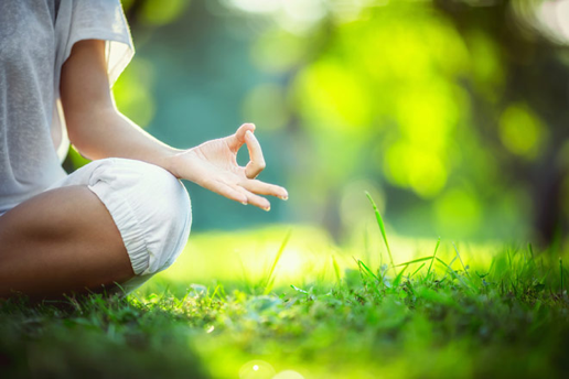 A woman is sitting in a lotus position in the grass.