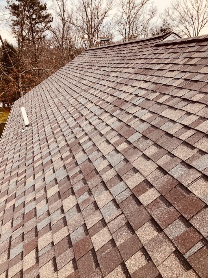 Rooftop covered in brown and gray shingles with trees in the background