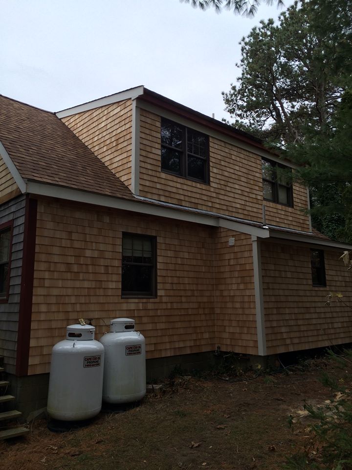 Two-story house with wood siding, black-trim windows, and propane tanks in the yard.