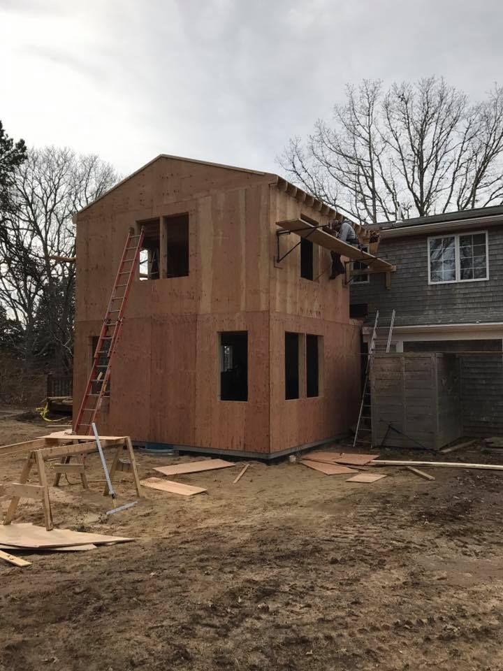 Partially built two-story wooden house under construction beside an older house