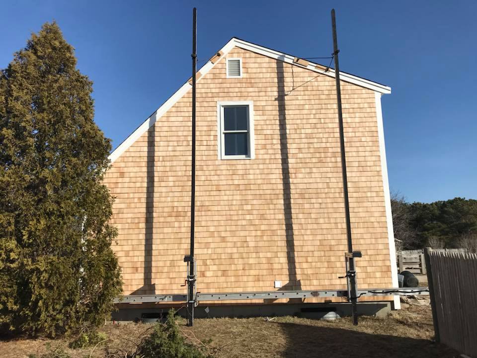 Small tan house exterior with white trim and scaffolding under a clear blue sky