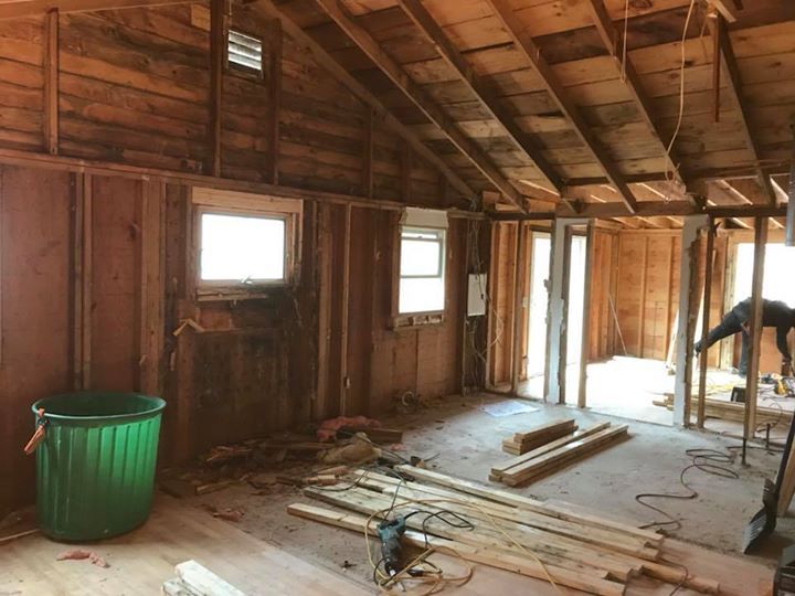 Unfinished attic with exposed beams, small windows, debris on the floor, and a green trash bin.