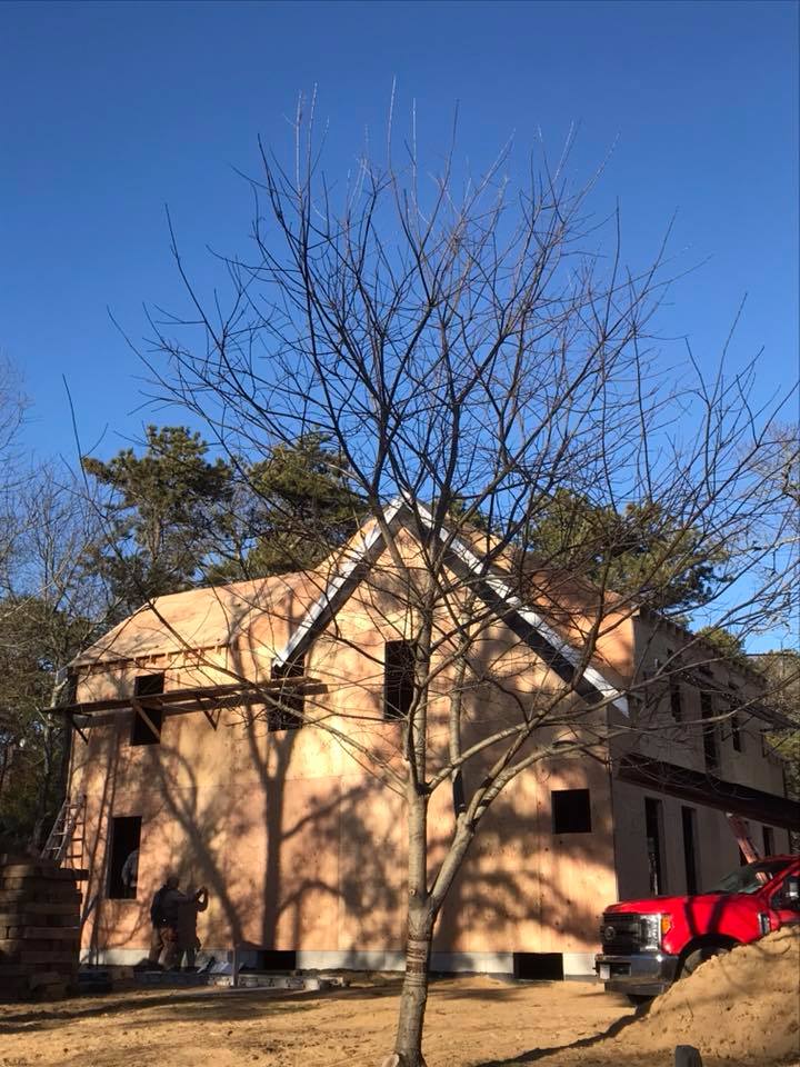 Two-story beige house with a leafless tree in front and a red truck parked beside it.