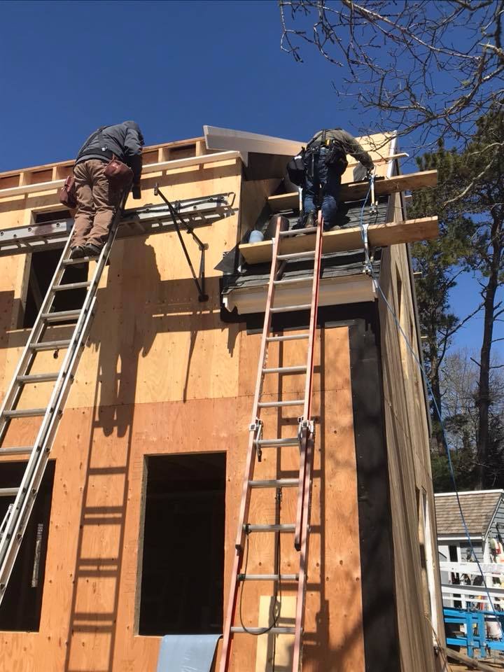 Two workers on ladders installing roof framing on a wooden house under construction.
