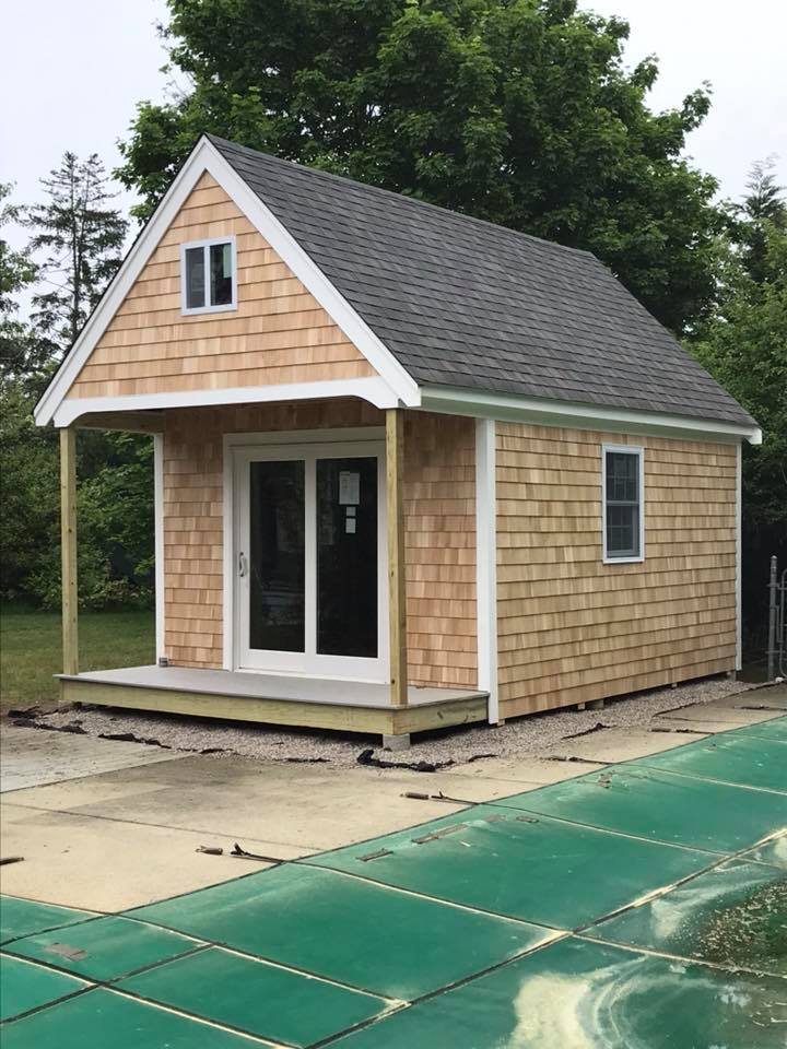 Small tan cottage with gray roof and white trim on a concrete pad outdoors