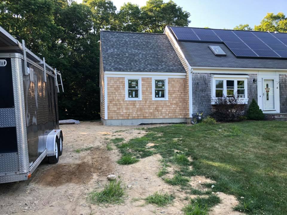 A house with solar panels and a gravel driveway beside a parked trailer and grassy yard.