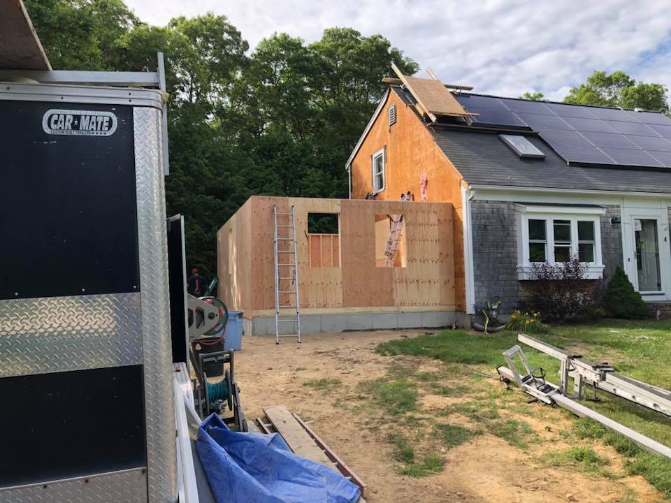 House under renovation with new plywood wall framing and roof work, construction trailer on the left.