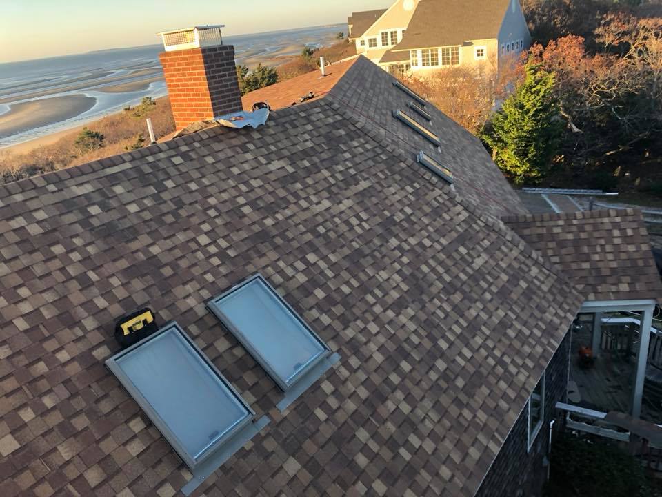 Rooftop with brown shingles, two skylights, and ocean view at sunset