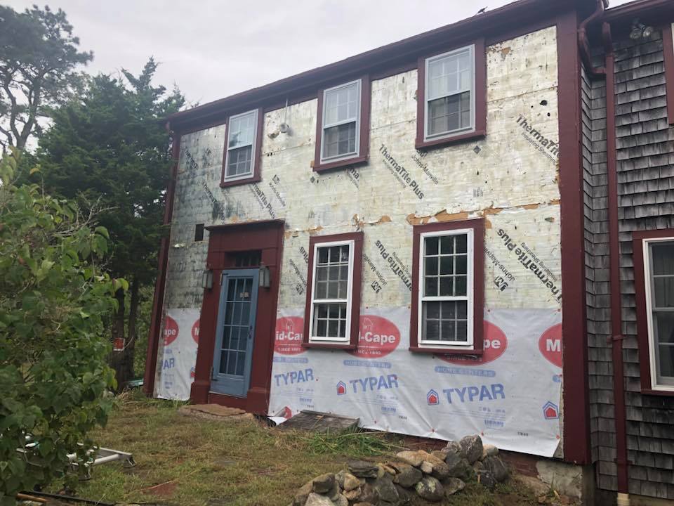 Old two-story house with red-trim windows and unfinished white siding under renovation