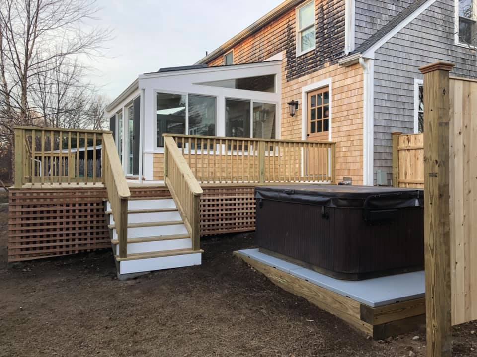 Back deck with white steps, wooden railings, and a hot tub beside a brick house