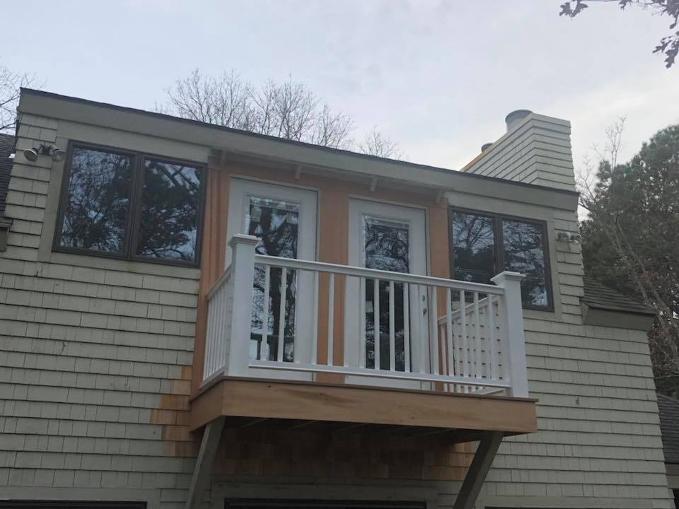 Second-story balcony with white railing on a gray-shingled house exterior