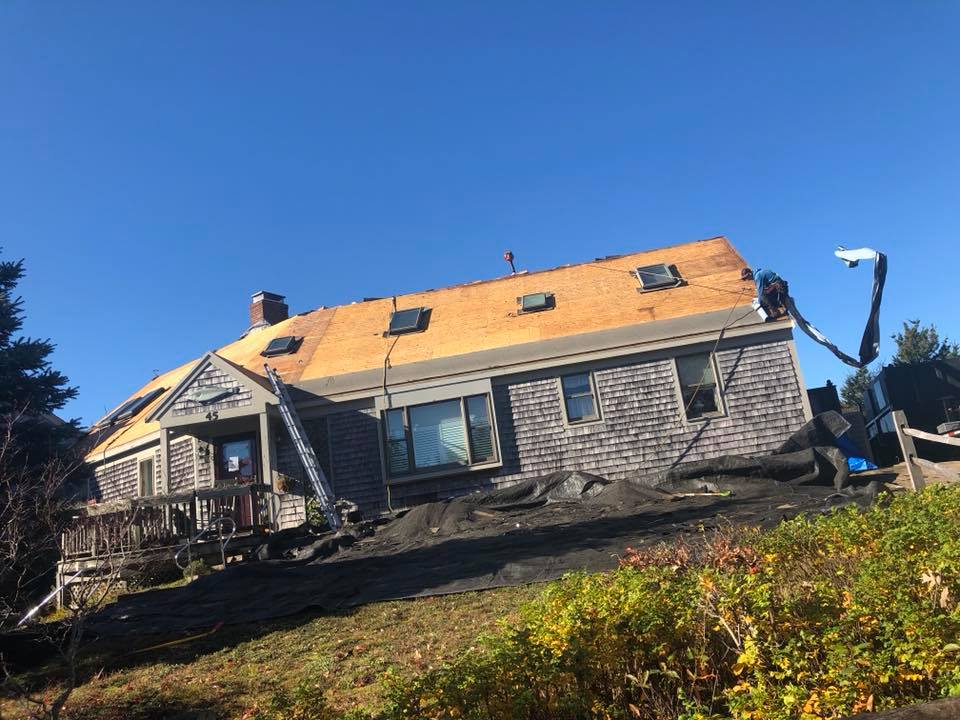 Tilted house with orange roof and gray siding on a grassy slope under a clear blue sky