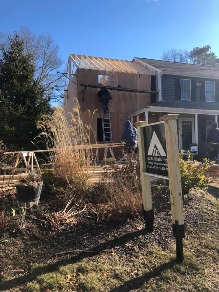 Worker installing roof on a house under construction beside an A-frame sign and tall grass