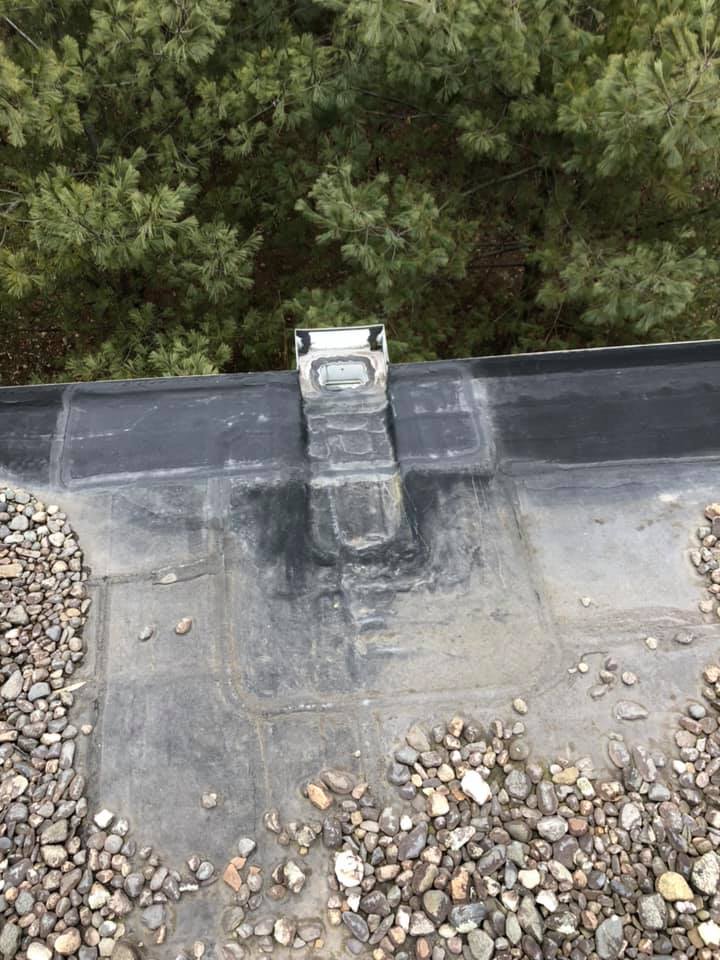 Roof drain with metal scupper and gravel edging on a flat black membrane roof
