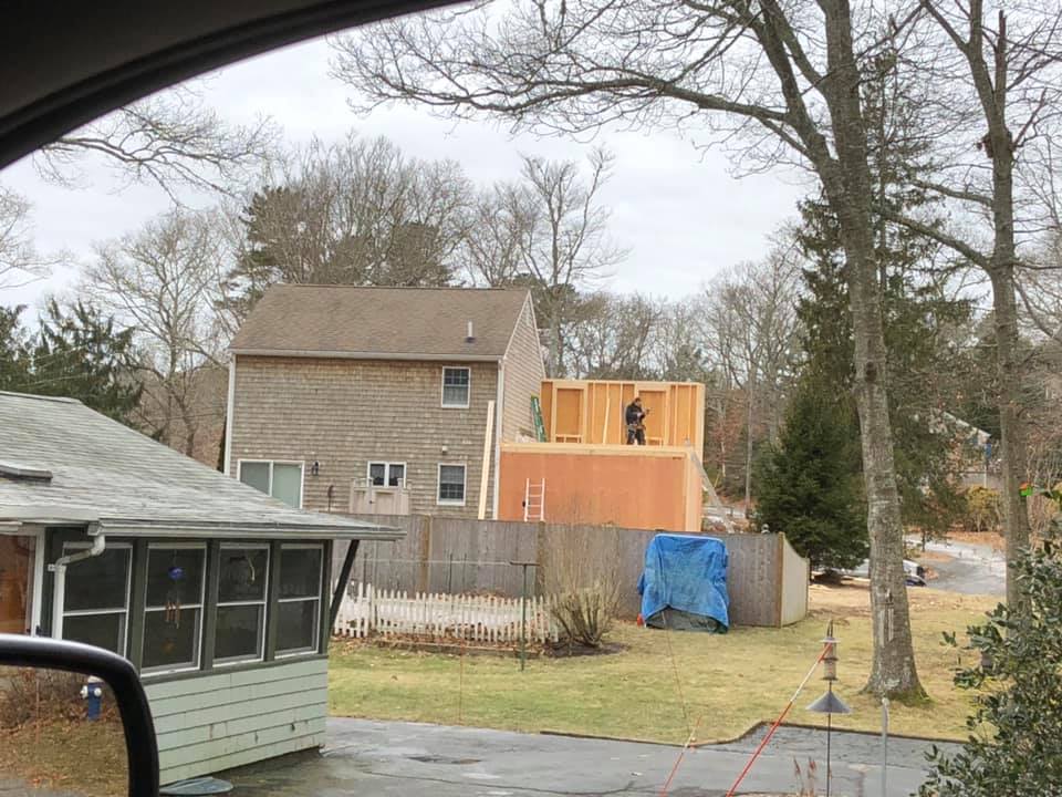 Suburban backyard with a house, unfinished wooden deck, trees, and a blue tarp by the fence