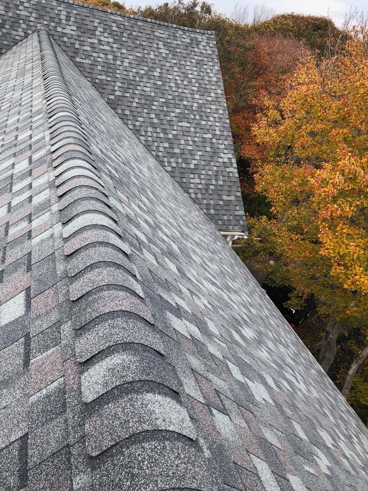 Steep gray shingled roof beside autumn trees with orange and yellow leaves