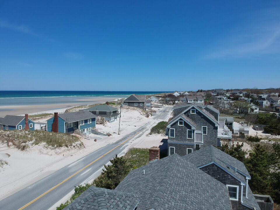 Coastal neighborhood with beach houses, road, dunes, and blue ocean under a clear sky