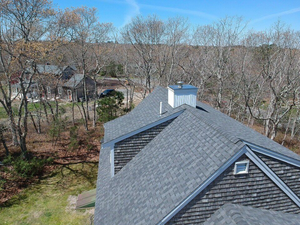 Rooftop with gray shingles overlooking leafless trees and a quiet residential street on a clear day