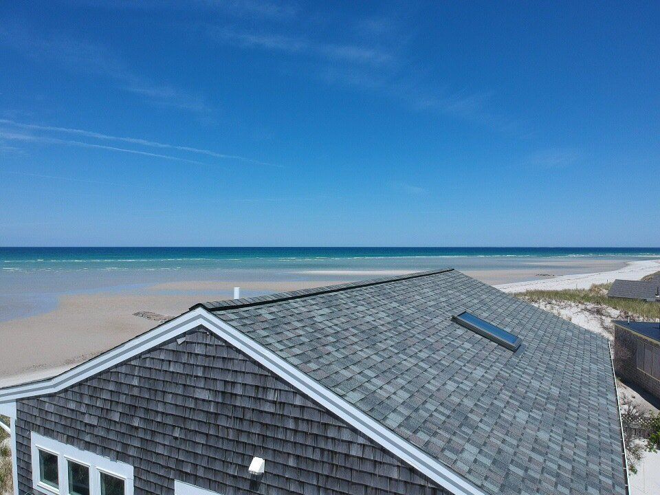 Coastal house roof with skylight overlooking a sandy beach and blue ocean under a clear sky
