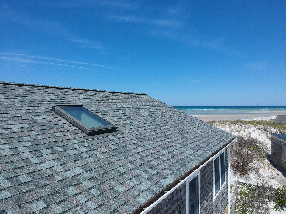 Beach house roof with skylight overlooking sand dunes and ocean under a blue sky