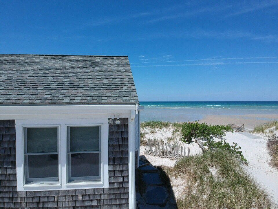 Beach house beside sand dunes and blue ocean under a clear sky.