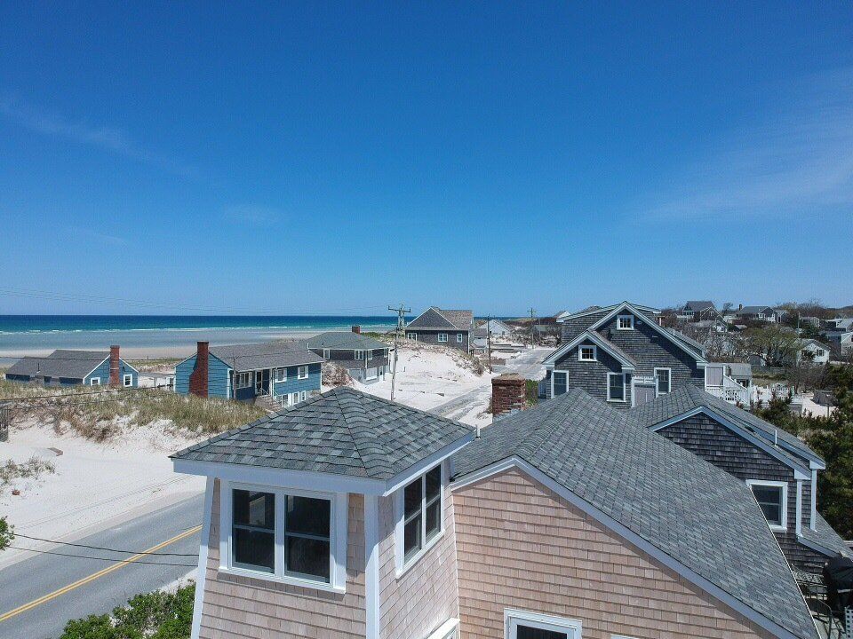 Beach houses and dunes under a clear blue sky, with the ocean in the distance.