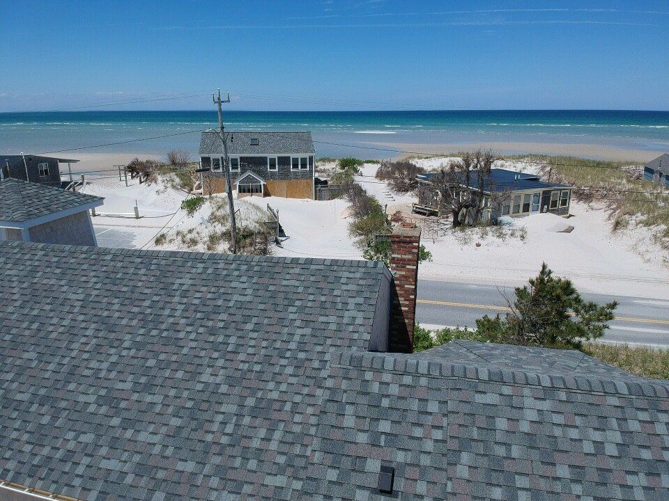 Beachfront houses and rooftops overlooking white sand dunes and turquoise ocean under a clear sky