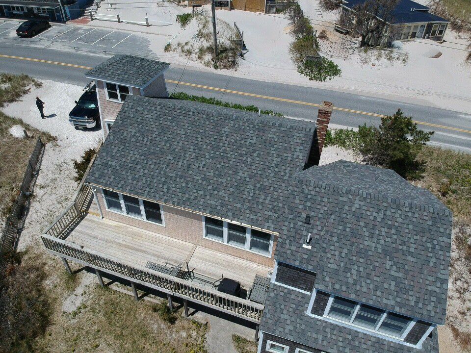 Aerial view of a gray-shingled house with a deck and snowy yard near a street
