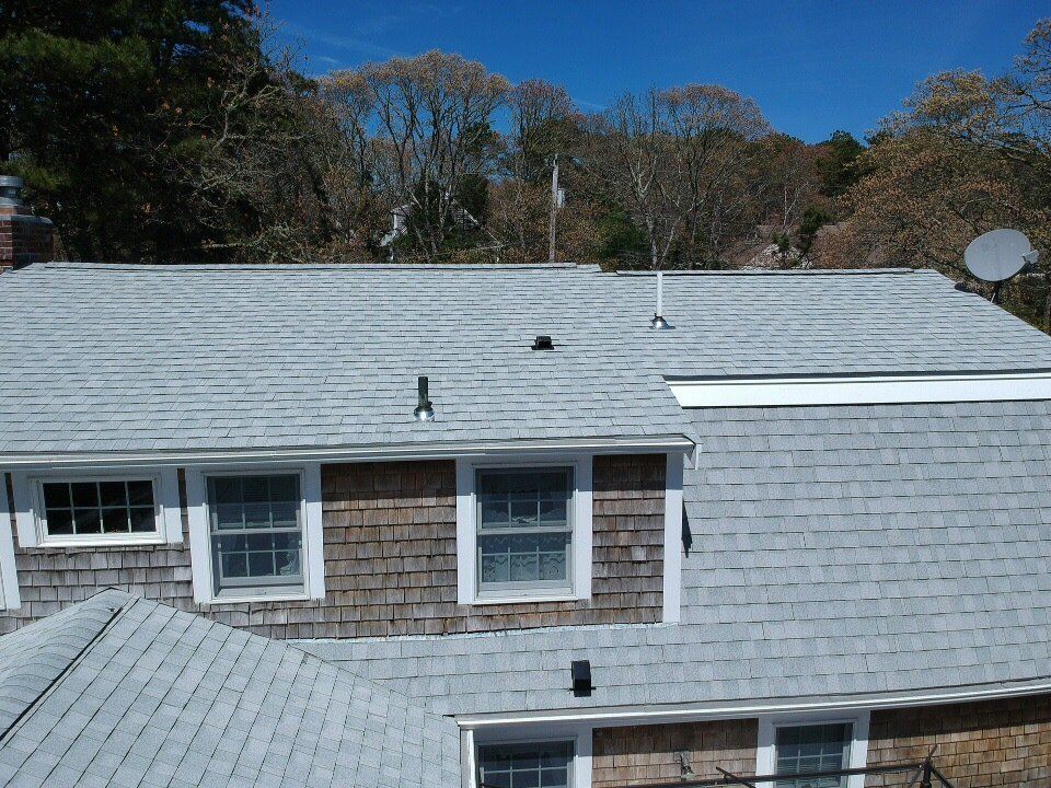 Gray shingled rooftop with dormer windows under a clear blue sky, trees in the background