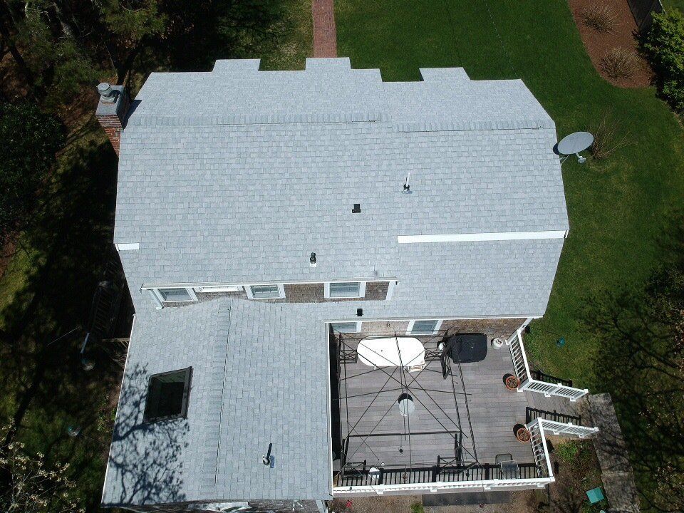 Aerial view of a white-roofed house with a backyard patio and surrounding green lawn.