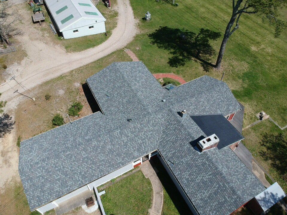 Aerial view of a single-story house with gray shingles and a red front porch in a rural yard