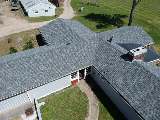 Aerial view of a gray-shingled house with a red door and grassy courtyard