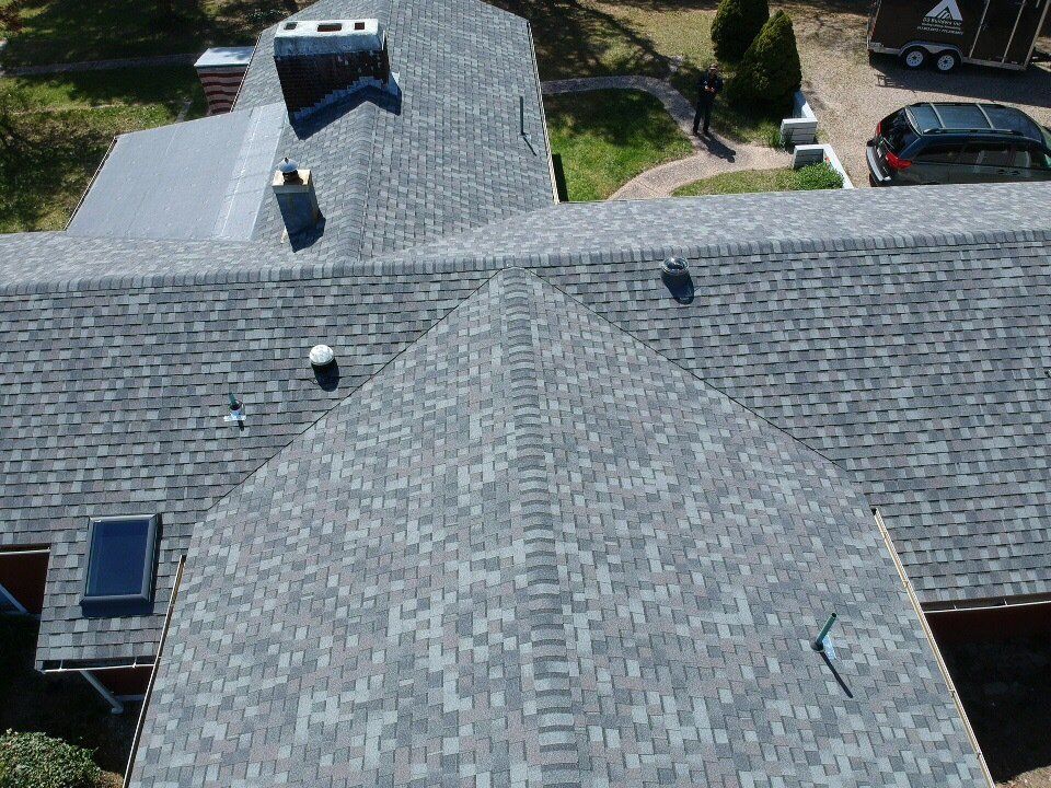 Aerial view of gray shingled house roof with skylights and parked cars nearby.