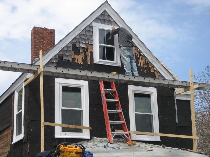 Worker repairing roof on a house with red ladders and exposed siding