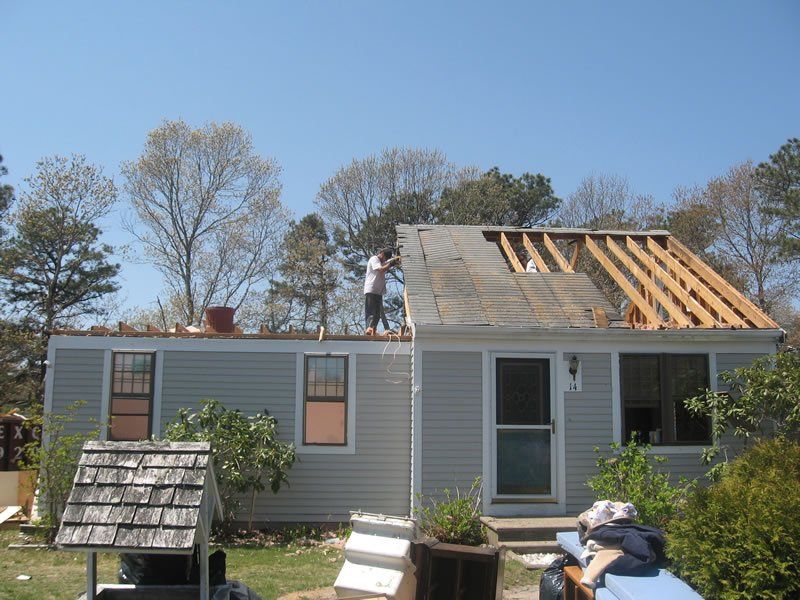 House with roof under repair and workers on top, with ladders and debris in the yard