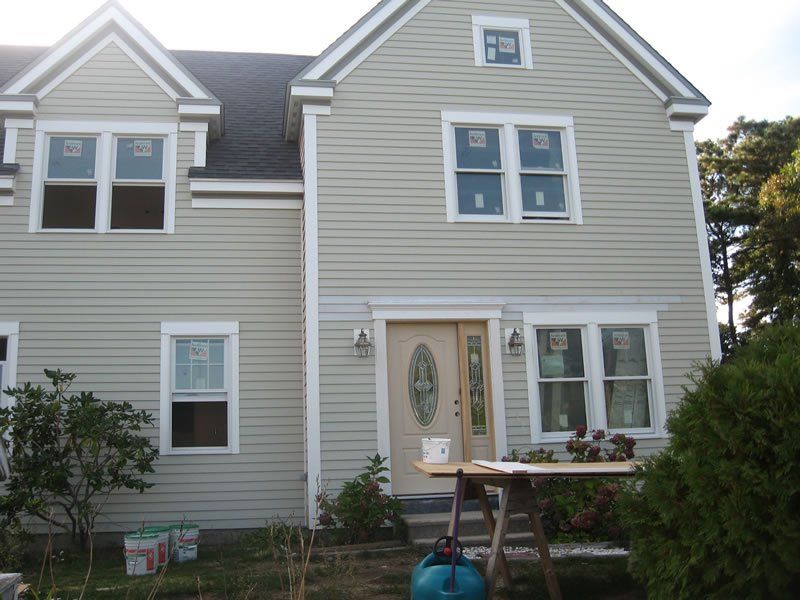 Two-story beige house with white trim, front porch, and a small table in the yard.