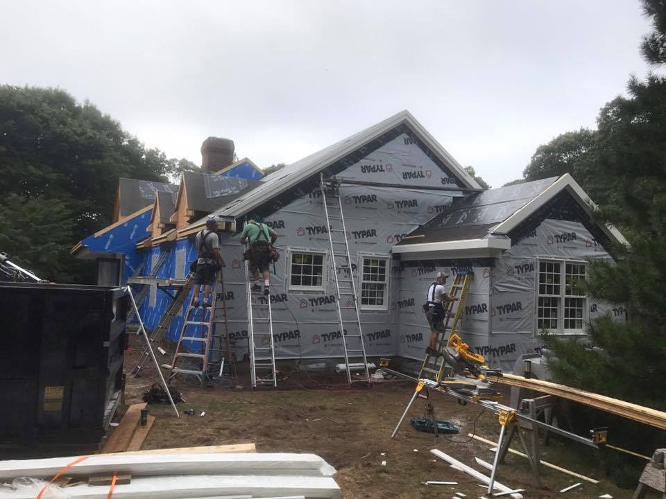 House under renovation with workers on ladders and scaffolding in the yard